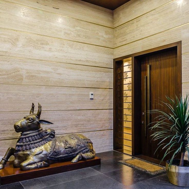 Luxury foyer interior in Indore featuring a bronze Nandi statue, wood panel door, and travertine marble walls.