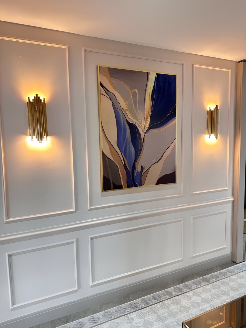 Elegant wall panel in Indore featuring classical molding, abstract art, and modern gold wall sconces.