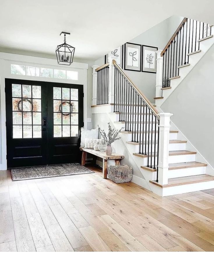 Modern farmhouse entryway and staircase in Indore featuring black double doors, wooden floors, and a staircase.