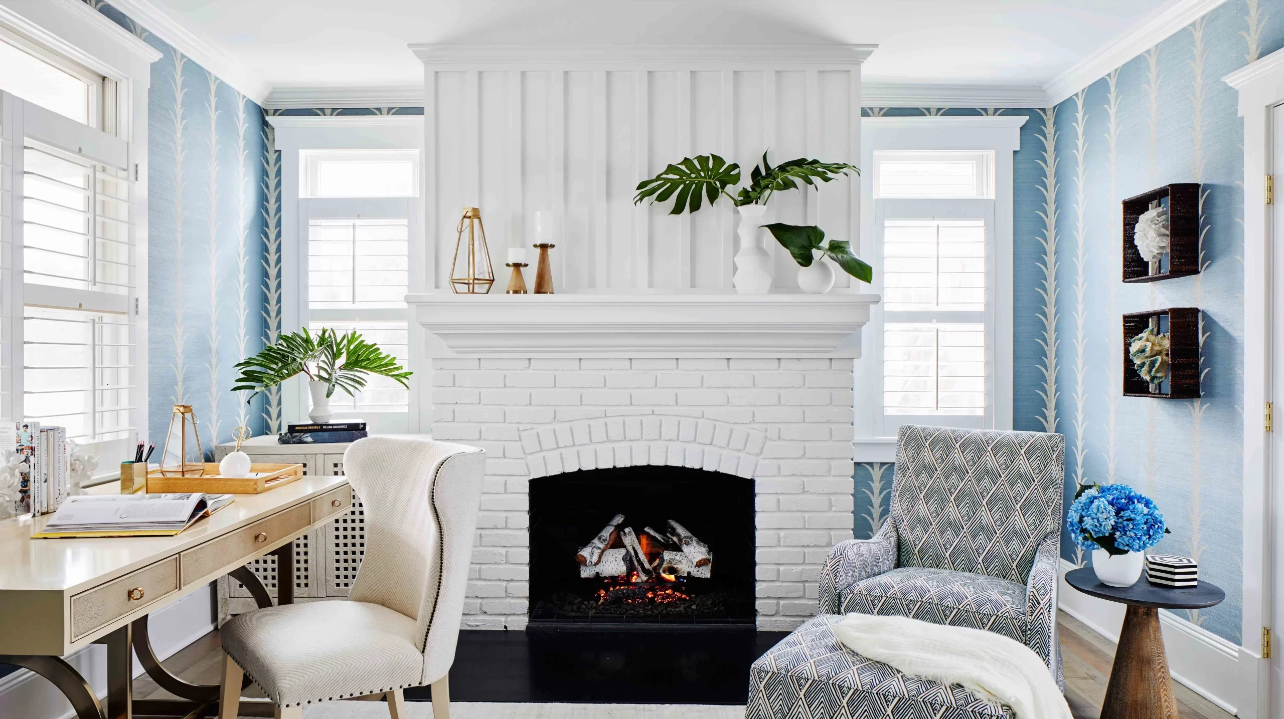 Elegant home office interior in Indore featuring blue patterned wallpaper, a white brick fireplace, desk, and armchair.