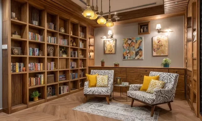 Luxury home library interior in Indore featuring floor-to-ceiling wooden bookshelves, patterned armchairs, and warm lighting.