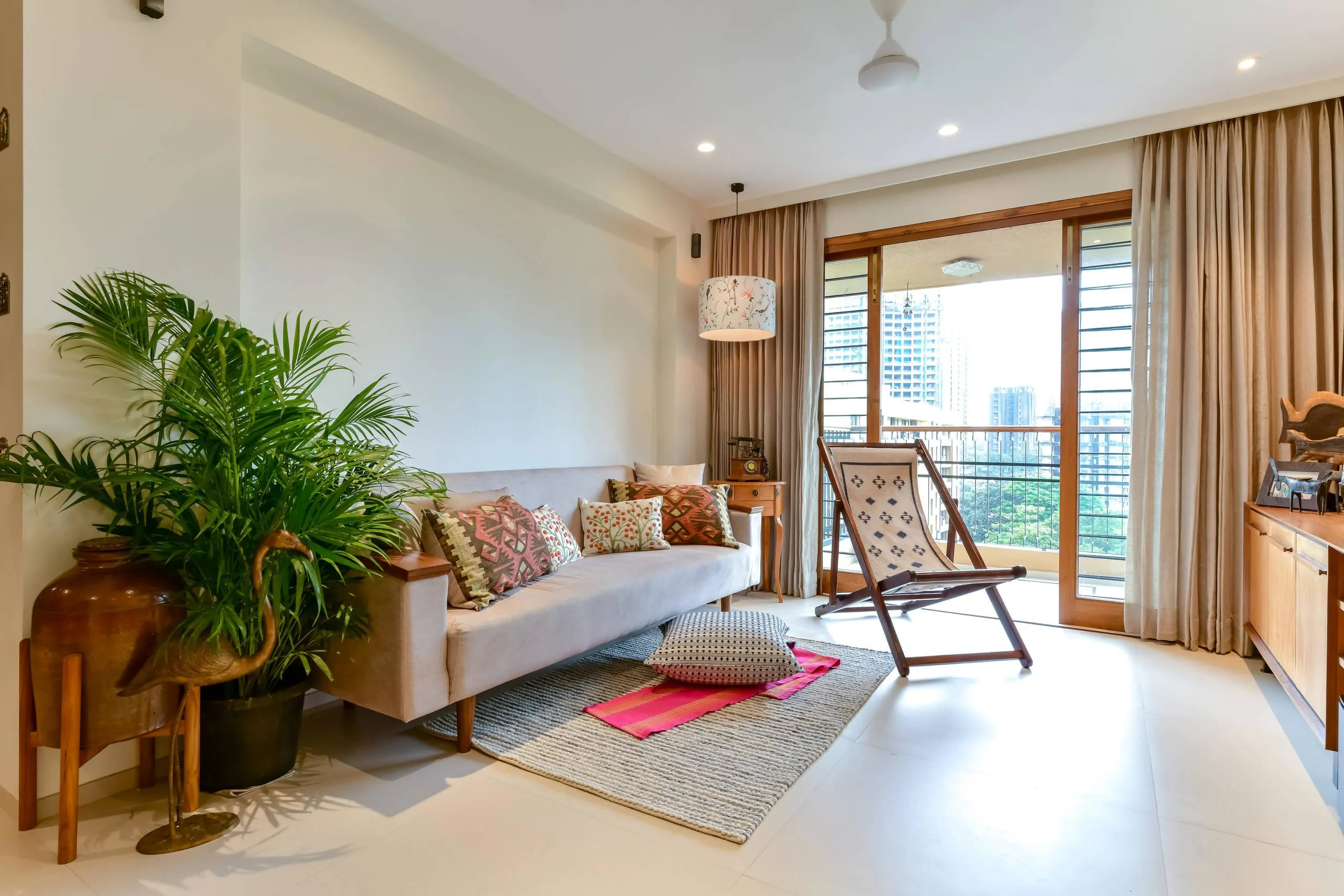 Modern Indian living room interior in Indore featuring a sofa with ethnic cushions, indoor plants, and a balcony view.