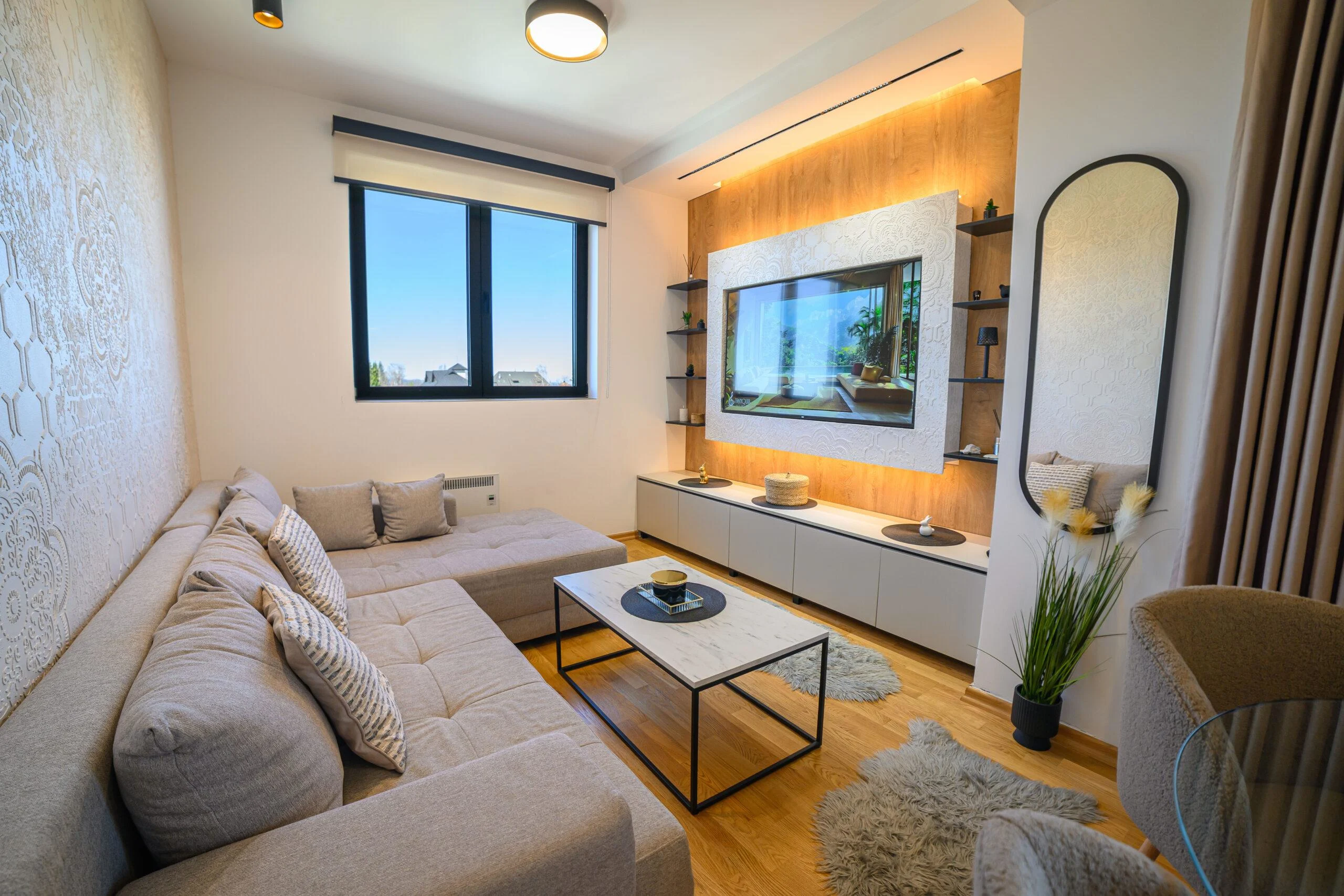 Modern cozy living room interior in Indore featuring a sectional sofa, TV wall panel with backlighting, and coffee table.