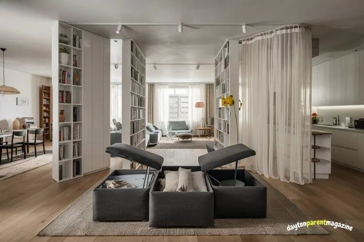 Modern open-plan living space in Indore featuring built-in bookshelves, storage ottomans, and room dividers.